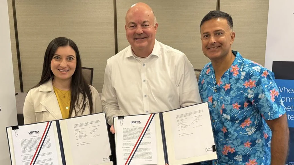 Three adults smile while holding open folders with official documents in a meeting room.