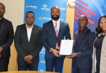 Telecom Namibia Fast-Tracks Fibre Links with Lightstruck Five professionals in business attire stand together; the two men in the center exchange a certificate in front of a Telecomm Namibia backdrop.