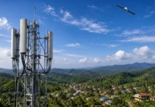 Malaysia Explores Starlink Satellite to Phone Service to Improve Rural Connectivity Telecommunications tower with multiple panel antennas on a hillside overlooking a valley with a small village beneath, under a blue sky with a satellite nearby.