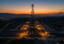 Deal to Launch First Kurdish Conversational AI Platform Telecommunications tower surrounded by satellite dishes at a fenced facility on a hill at sunset.