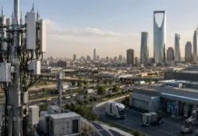 Zain KSA Starts Commercial 5G-Advanced Network Rollout Telecom antenna tower on a rooftop with a city skyline and highways in the background as the sun sets on a modern business district.