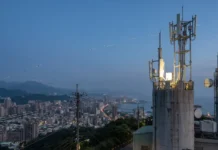 Taiwan Moves Closer to Starlink Satellite Internet City skyline at dusk with a tall telecom tower and antennas on a hilltop over the city and coastline beyond, including power lines in the foreground.