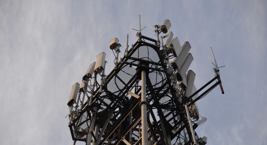 Cellular communication tower with multiple antenna panels against a clear sky.