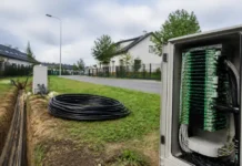 Deutsche Telekom Advances Fiberhost Inea Acquisition Outdoor telecom cabinet with green circuit boards and bundled cables beside a trench in a suburban street visualizing underground fiber deployment.