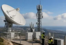 Satellite Network Partnership Expands Across Europe Large satellite dish and cellular antennas on a fenced hilltop, with two workers in safety vests inspecting equipment nearby.