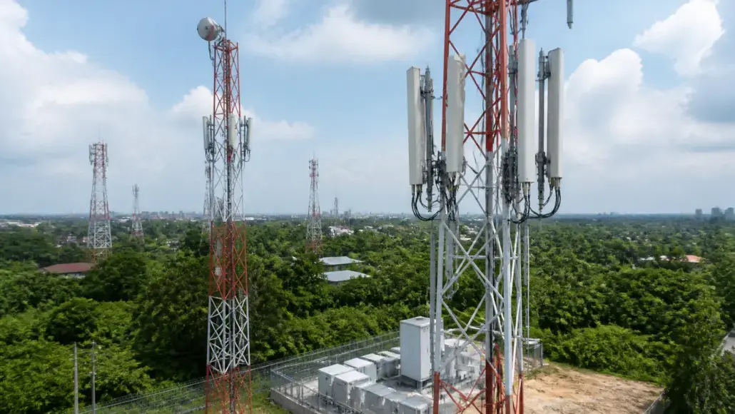 Cellular communication towers with antennas atop a fenced equipment pad in a green, suburban area