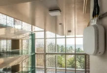 Cloud RAN Powers Multi-Operator Indoor Network in Saudi Arabia White wall-mounted wireless access point with exposed cables in a bright, modern building, large windows showing palm trees outside.