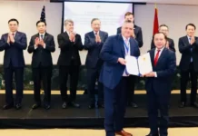 Satellite Network Testing Gets Green Light in Vietnam Two men in suits exchange a signed document on a stage as officials applaud in the background.