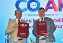 UK and Indian Telecom Industries Join Forces on Digital Fraud Two men in suits hold red COAI folders on a stage with a blue backdrop and COAI logo above them, mid-signing an agreement.