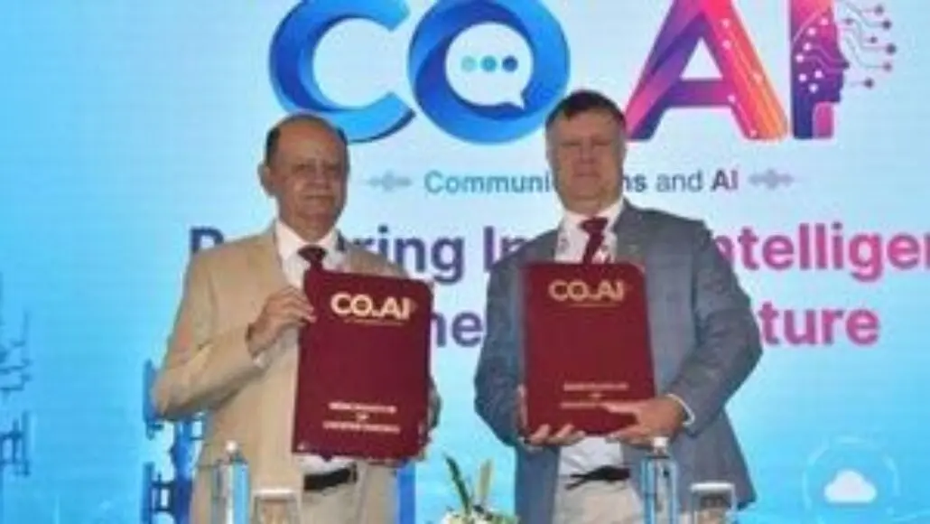 Two men in suits hold red COAI folders on a stage with a blue backdrop and COAI logo above them, mid-signing an agreement.
