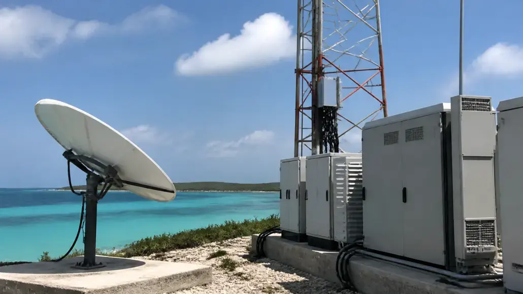 Satellite dish and telecom cabinets installed on a coastal site with turquoise ocean in the background